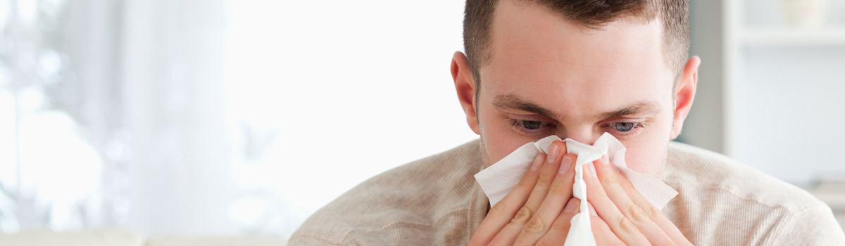 Young man with a beige sweater sitting on a cough blowing his nose