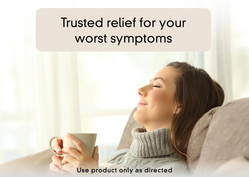 Woman leaning back on the couch with a blanket holding a hot beverage while her eyes closed
