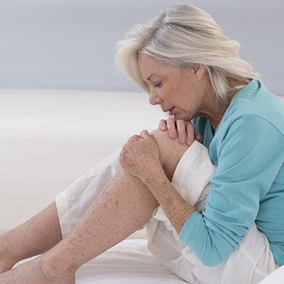 Older women sitting on the floor and holding her left knee with pain