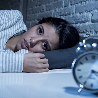 Woman lying in bed with her eyes open, and the clock showing the very early morning hours