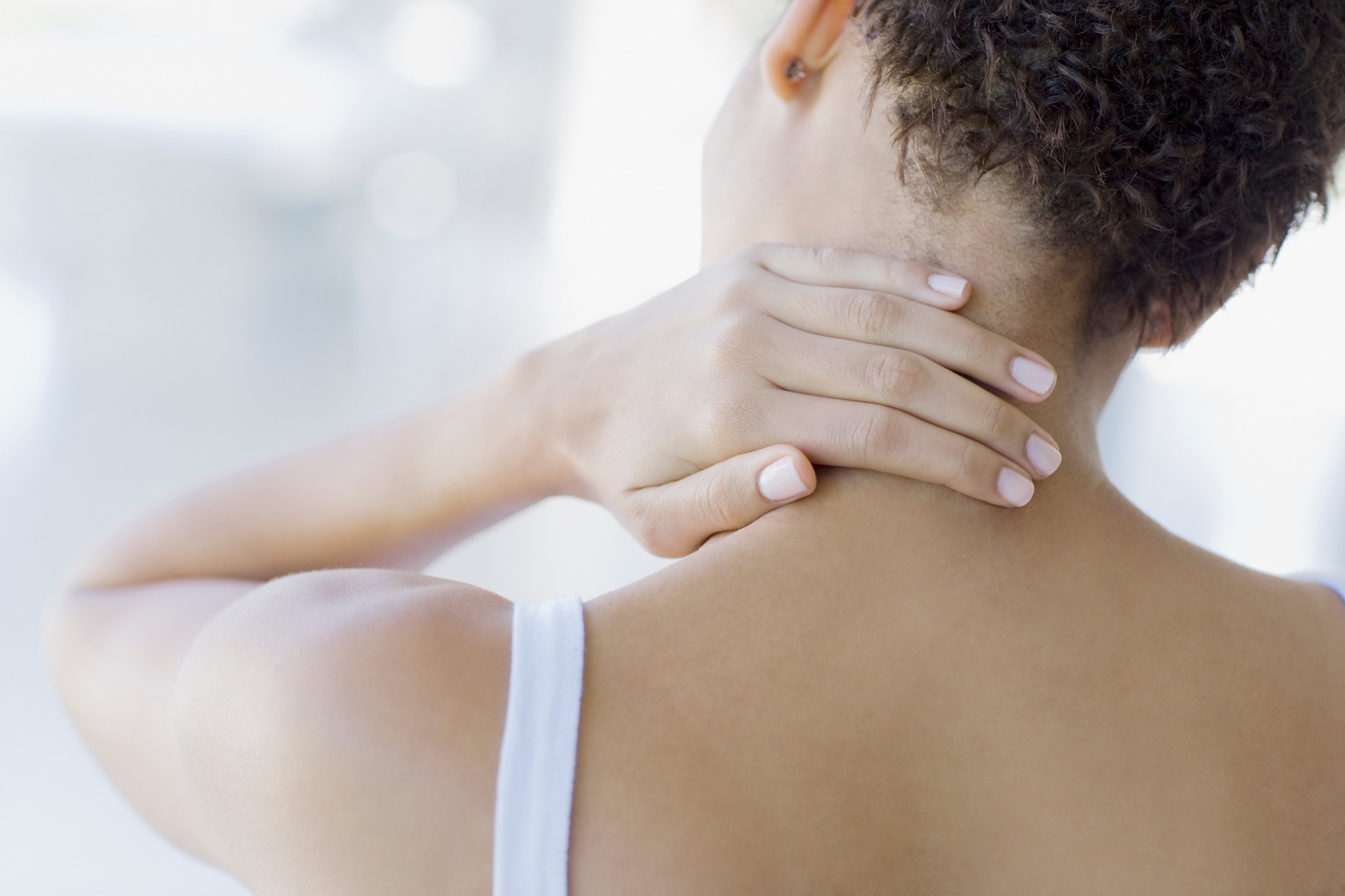 Woman who is experiencing muscle strain holding the back of her neck